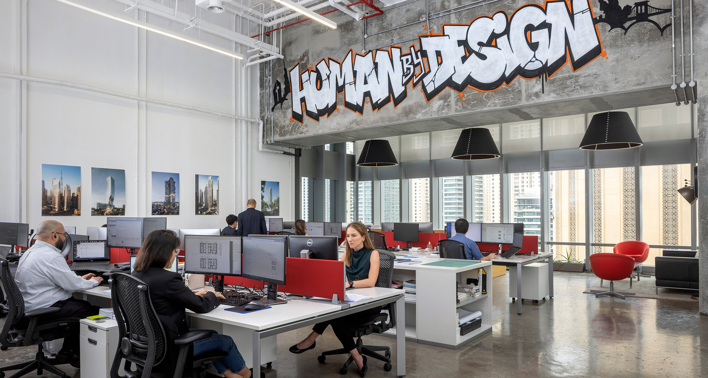 Perkins Eastman's Dubai studio staff working at the computers below Human By Design graffiti.